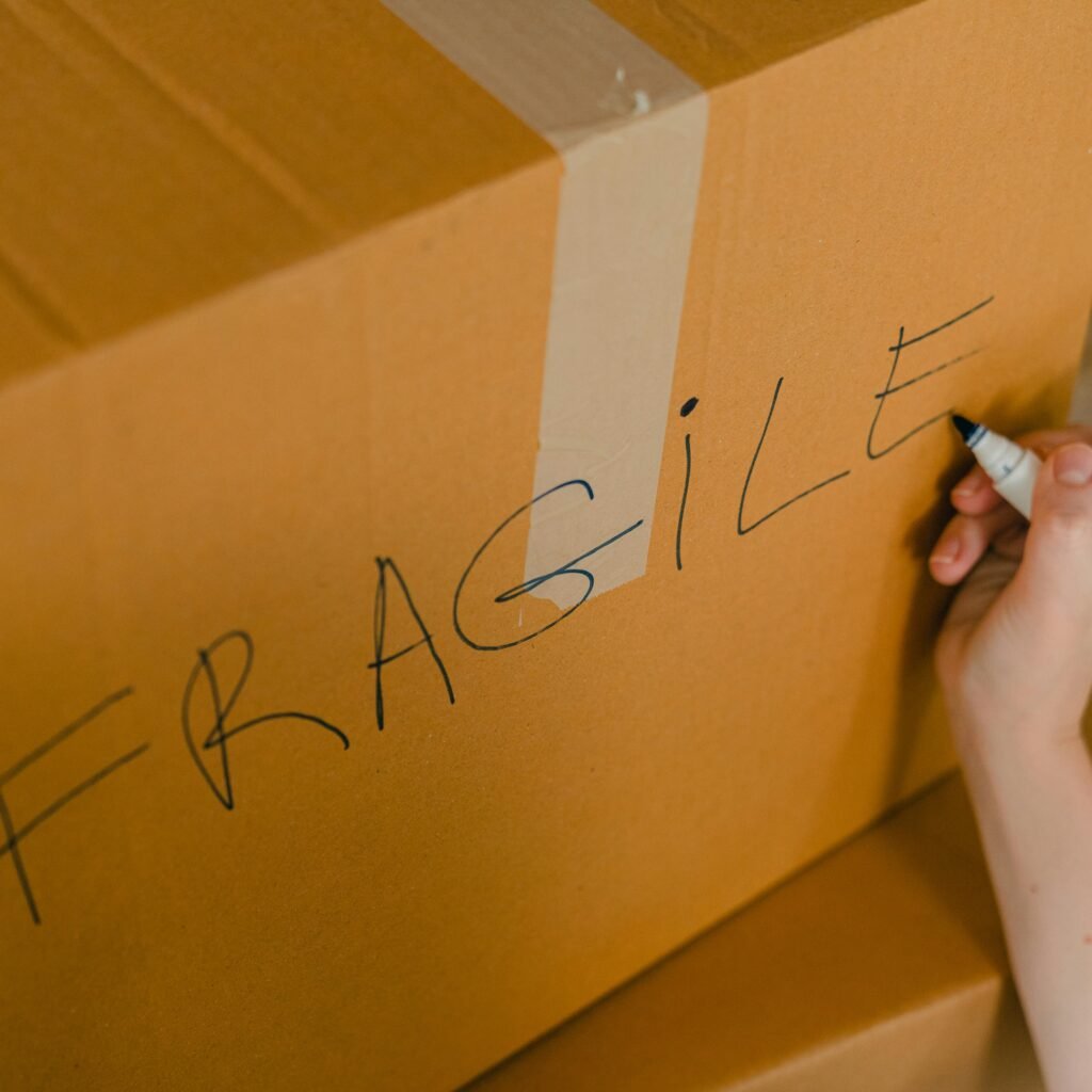 From above of crop unrecognizable person writing with marker on cardboard box with fragile products before relocation